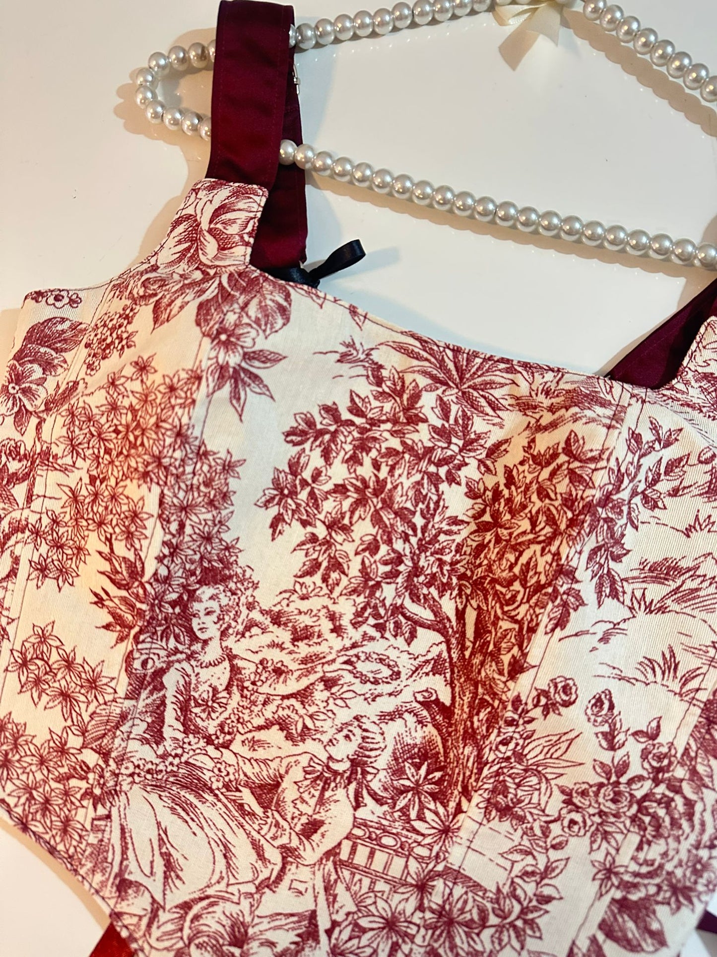 Red floral patterned corset top on a hanger with pearls