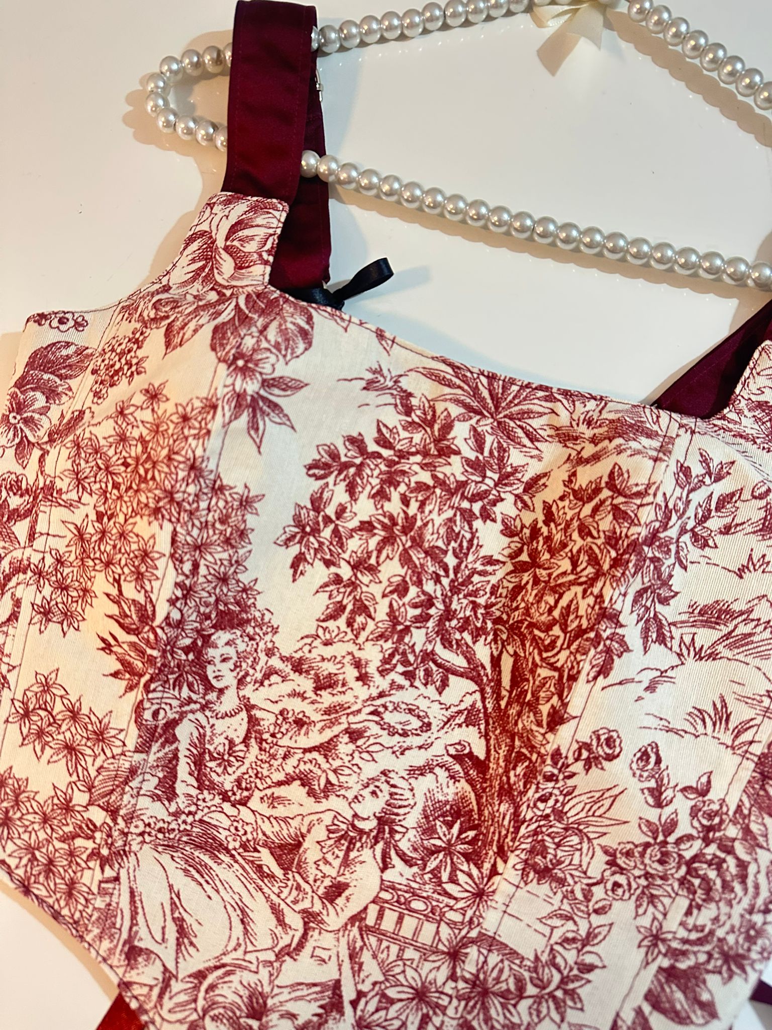 Red floral patterned corset top on a hanger with pearls