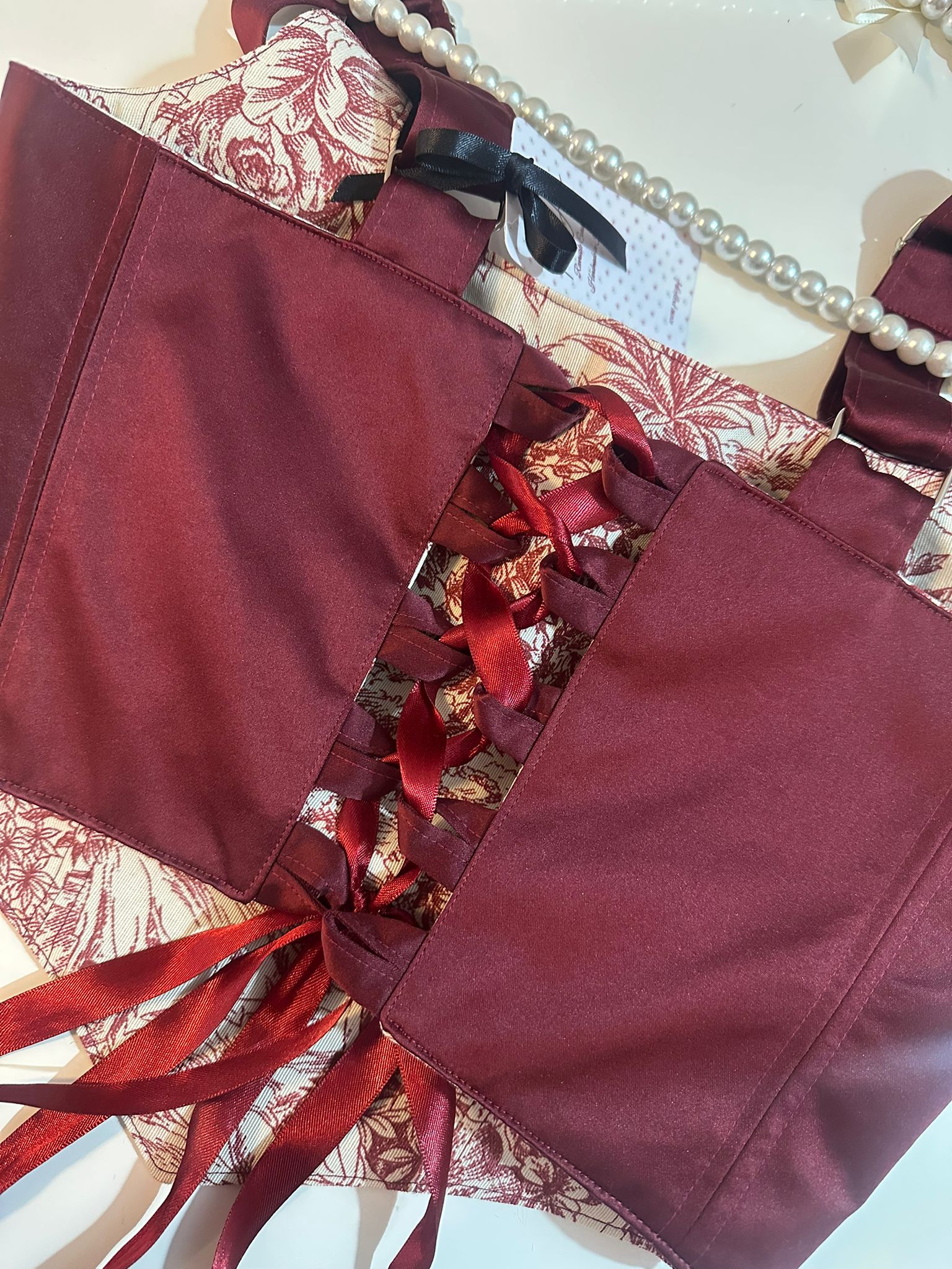 Burgundy corset top with red ribbons on a patterned background