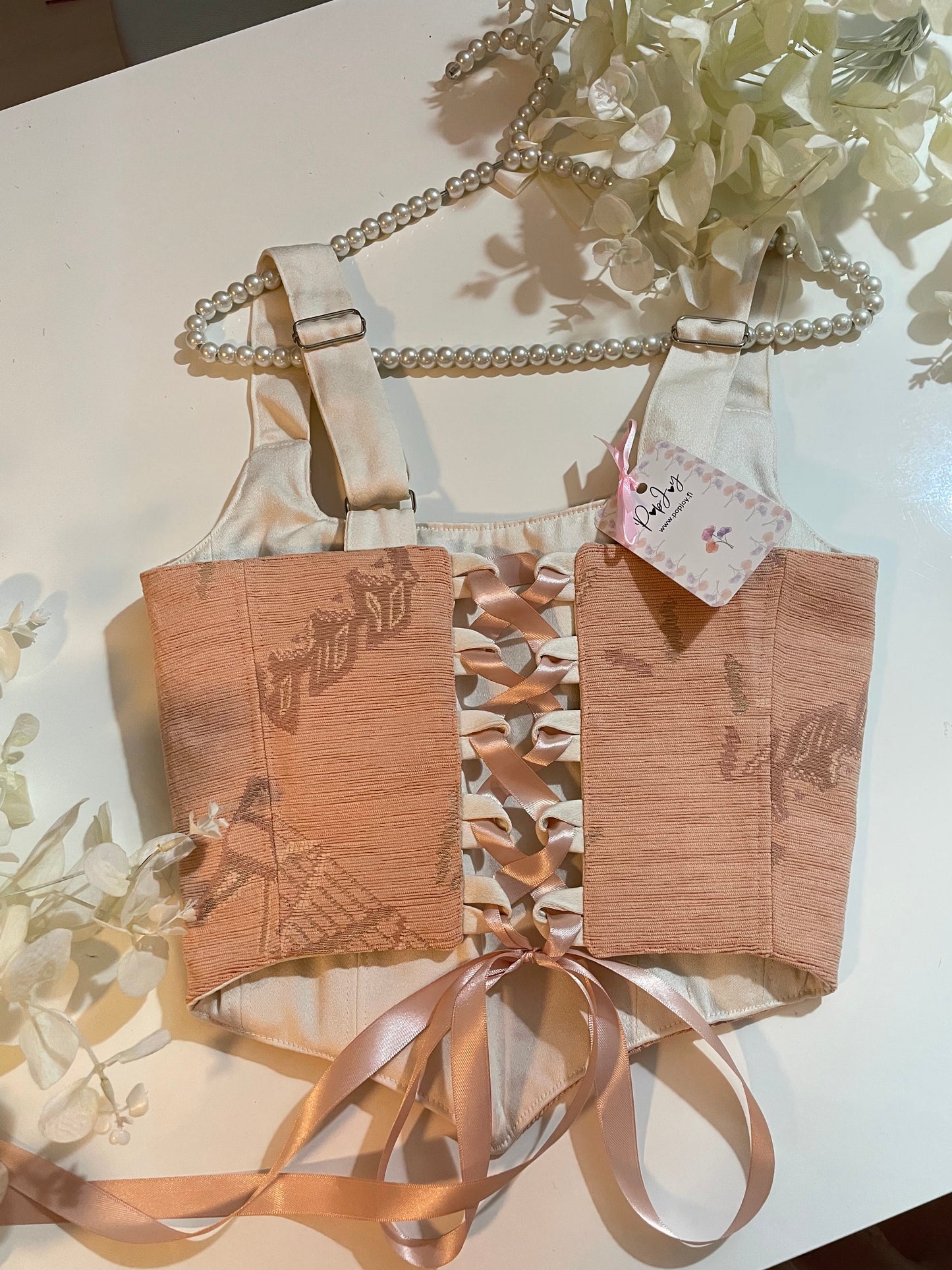 Bright-patterned corset top with white straps on a light surface with flowers.