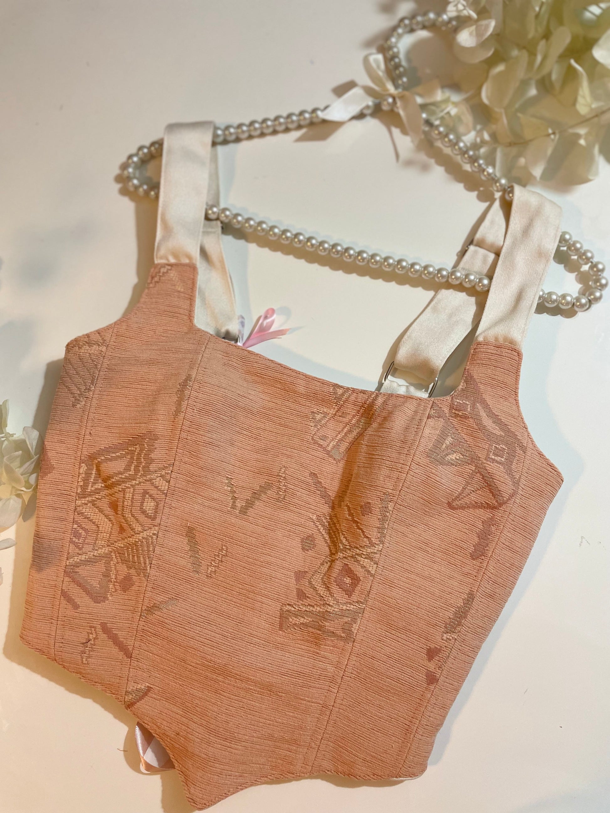 Brown embroidered corset top with a decorative bow on a light background