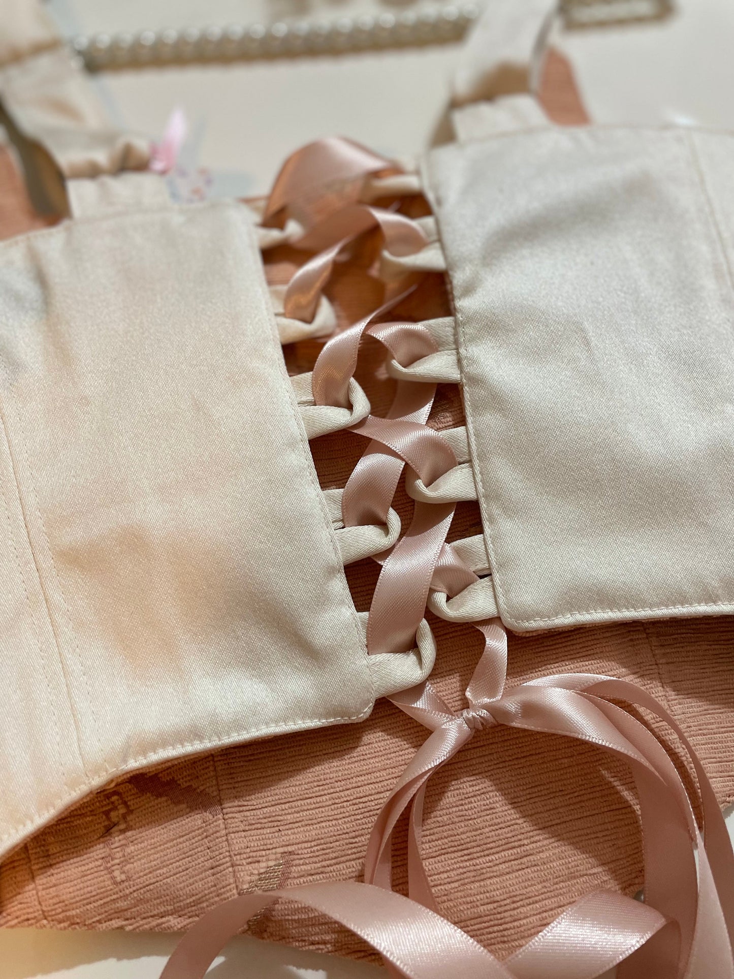 Close-up of beige corset top with pink ribbons on a textured fabric