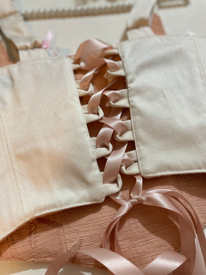 Close-up of beige corset top with pink ribbons on a textured fabric
