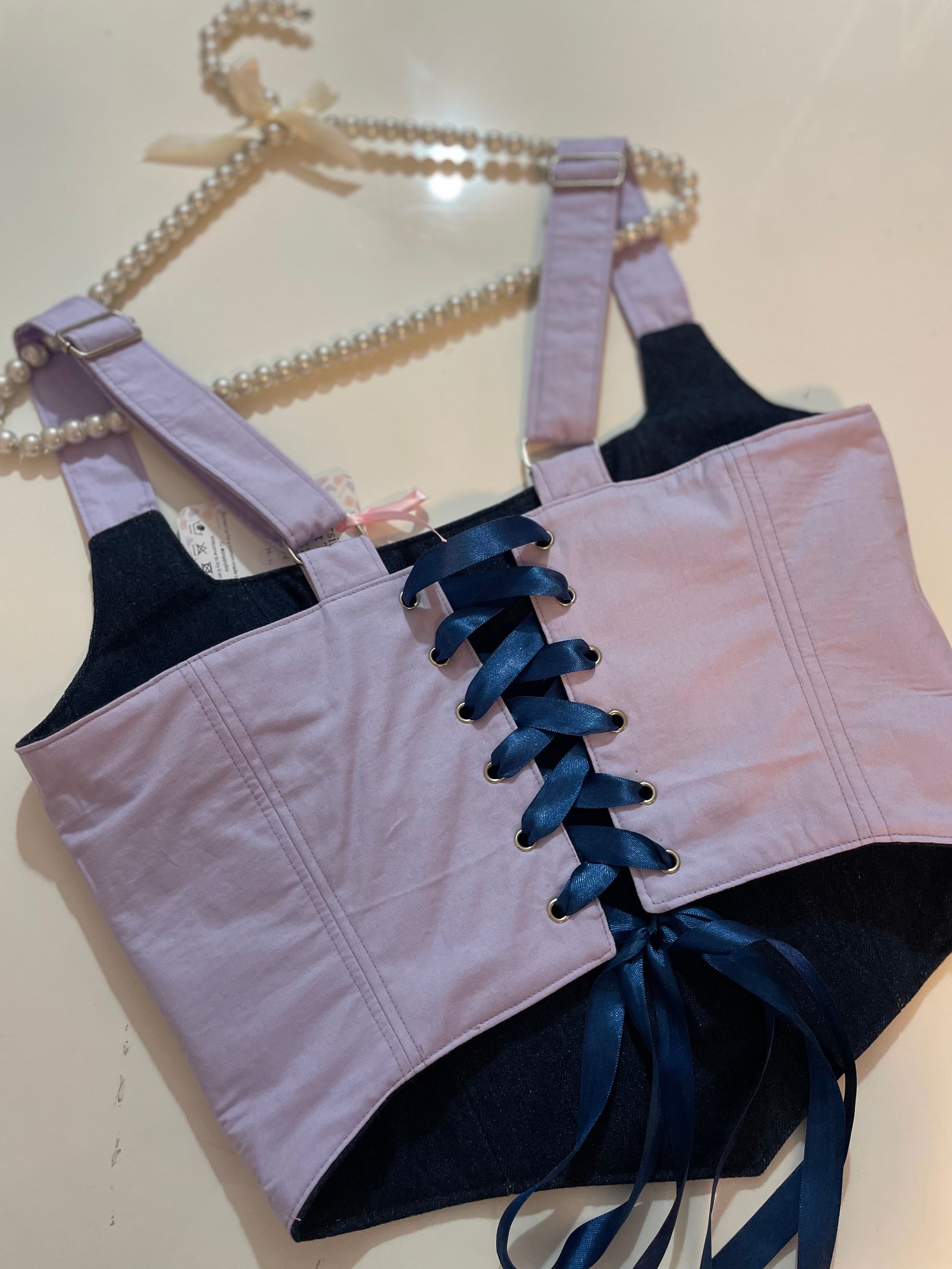 Light pink and blue laced ribbon corset top on a beige background