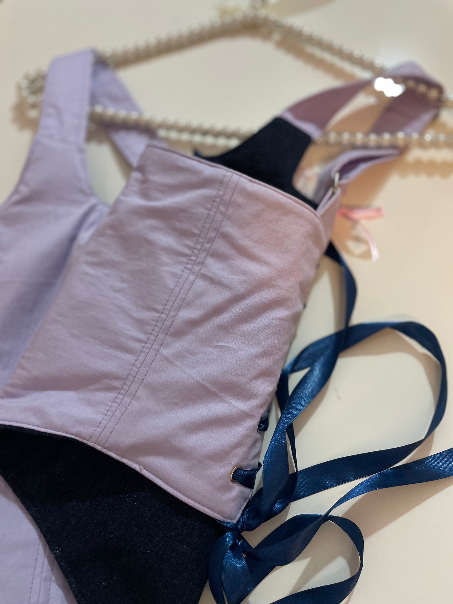 Light purple corset top with a blue satin ribbon on a beige background