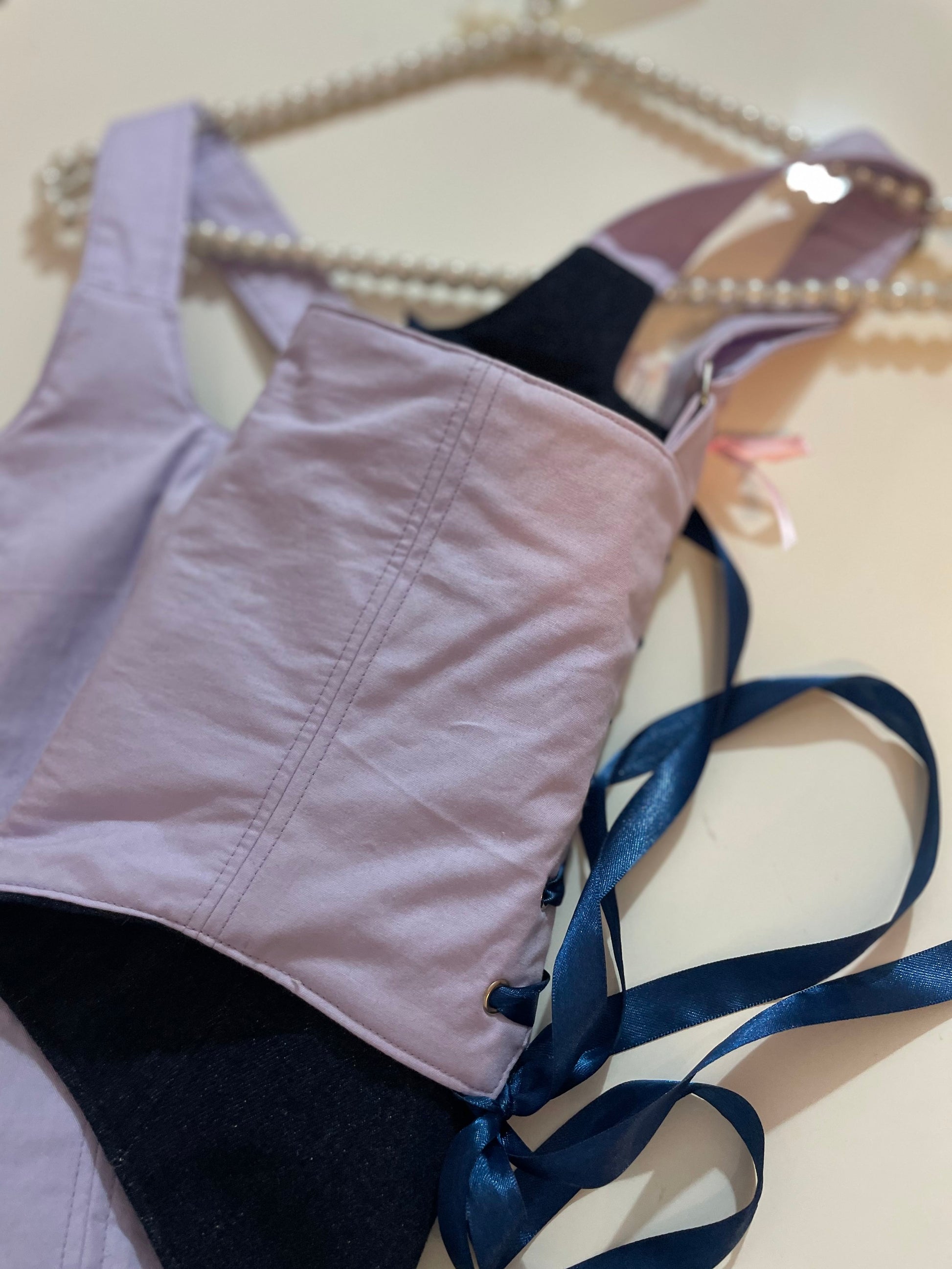 Light purple corset top with a blue satin ribbon on a beige background
