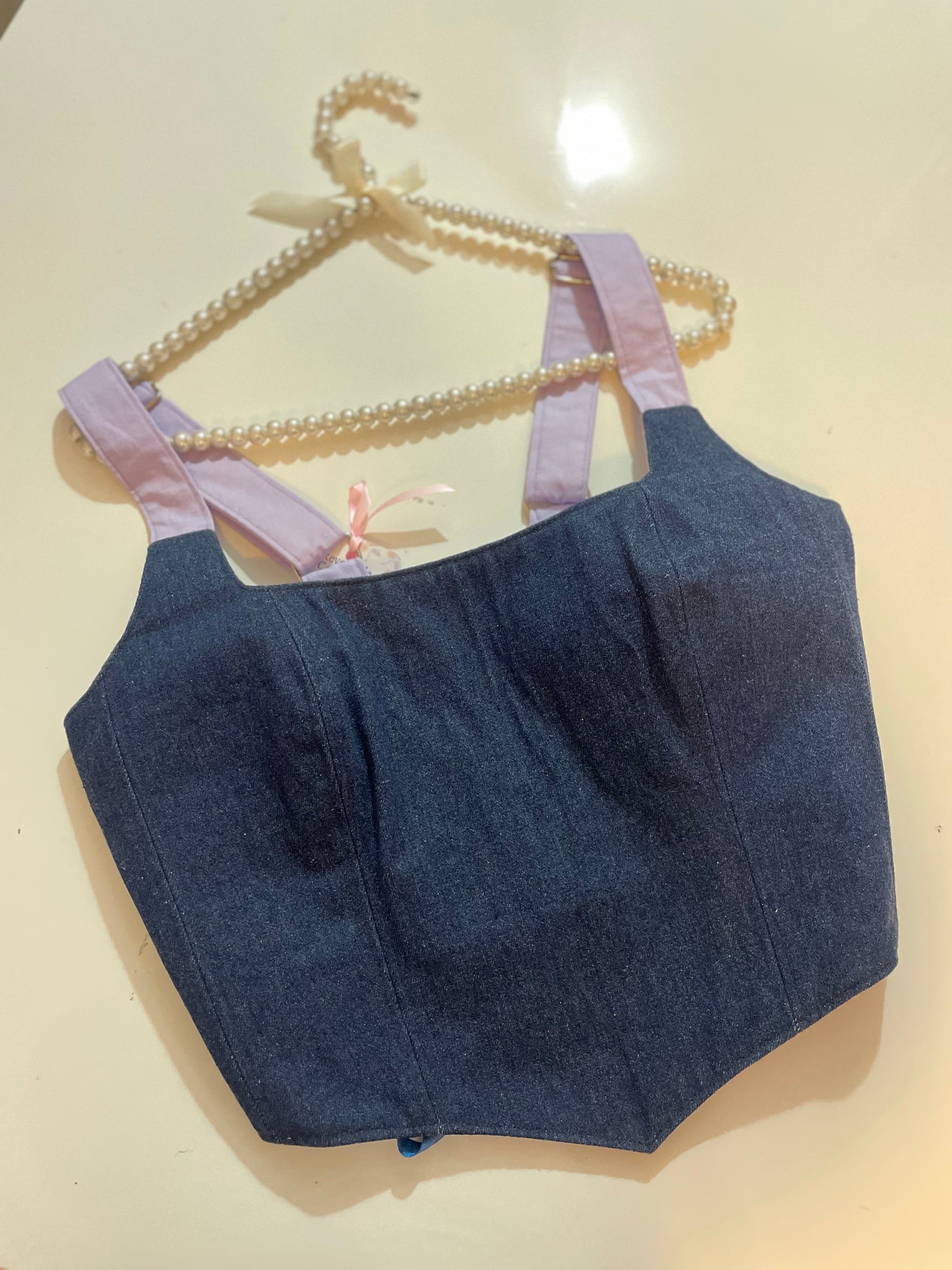 Denim corset top with pink straps on a beige background