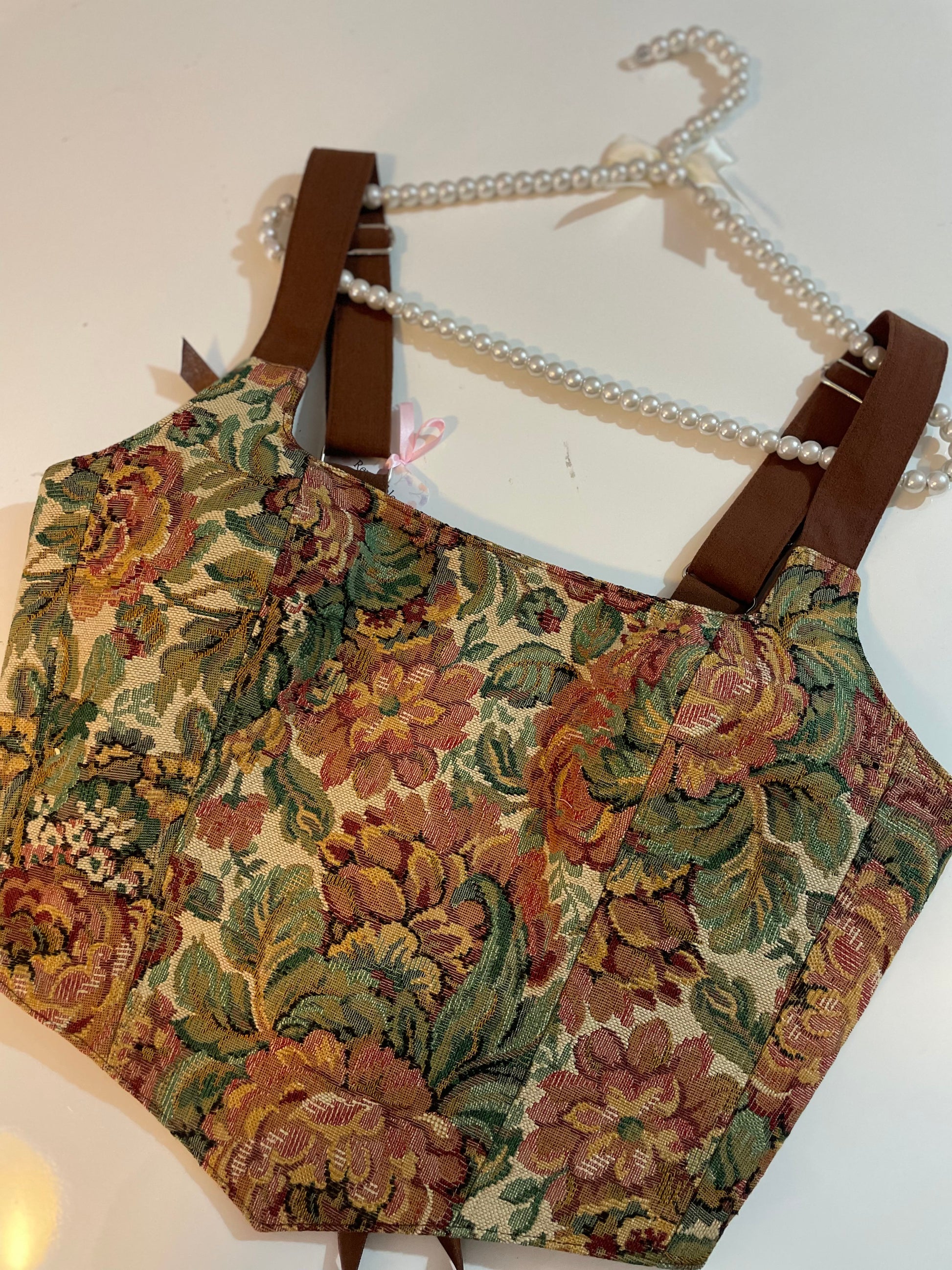 Floral-patterned corset top on a hanger with a pearls